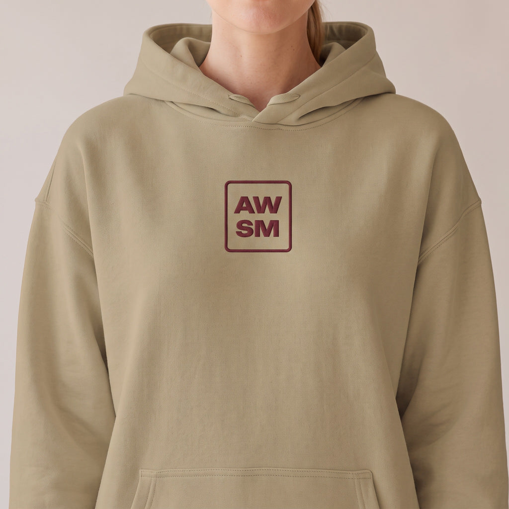 Bordeaux Relaxed Hoodie — AWSM Atelier in Dune Sand, close-up of the embroidered AW/SM badge on the AWSM house model