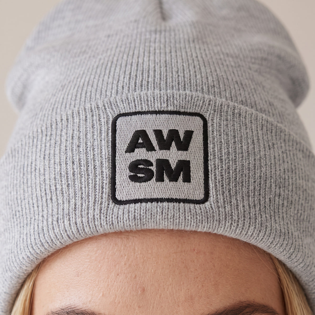 Neige Cuffed Beanie — AWSM Atelier in Cloud Heather Grey, close-up of the embroidery on the AWSM house model