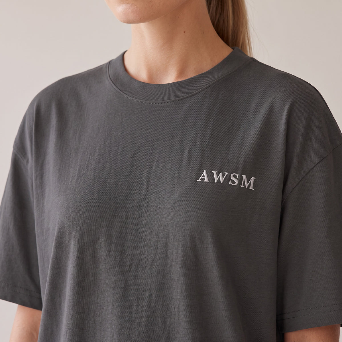 Patina Oversized Tee — AWSM Maison in Faded Onyx, close-up of the embroidery on the AWSM house model