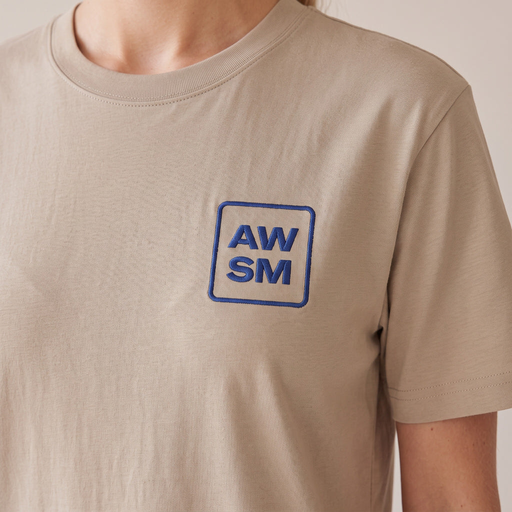 Terre Organic Tee — AWSM Atelier in Desert Dust, close-up of the embroidery on the AWSM house model