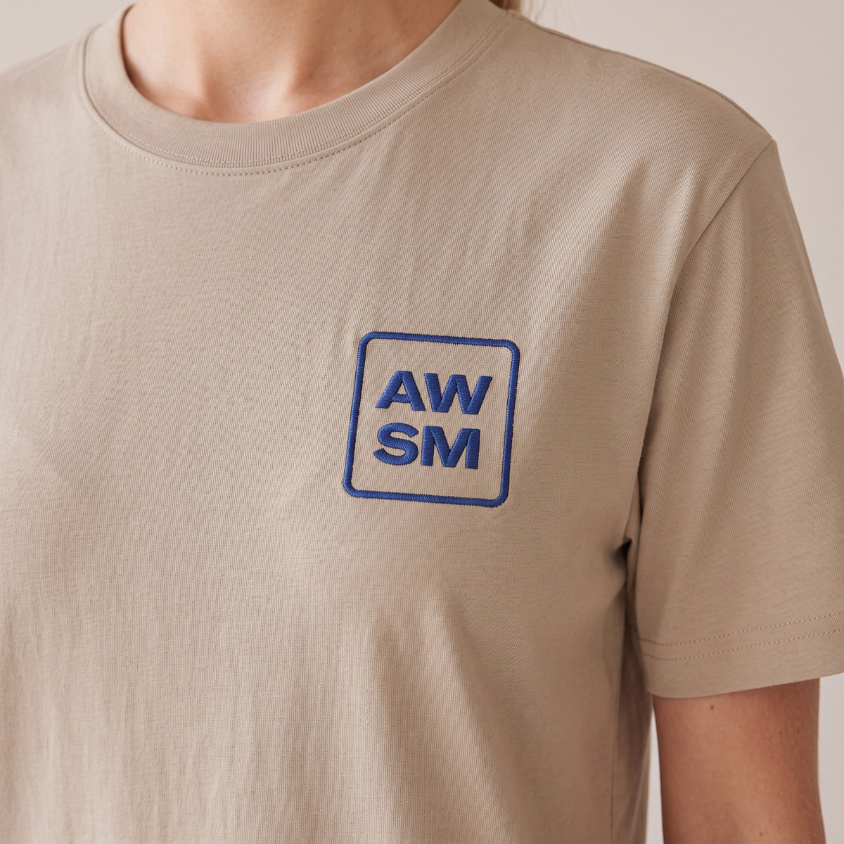 Terre Organic Tee — AWSM Atelier in Desert Dust, close-up of the embroidery on the AWSM house model